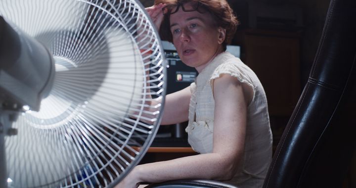 Woman is trying to work at the desktop computer at home, suffering from hot weather and using electric fan