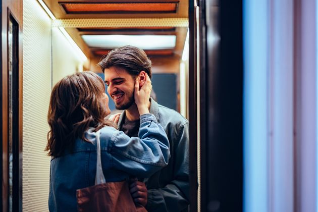 Smiling boyfriend kissing his girlfriend while embracing and laughing together in the elevator.