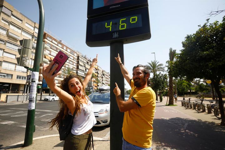 Unas personas se fotografían con un termómetro de calle que marca 46 grados en el centro de Córdoba