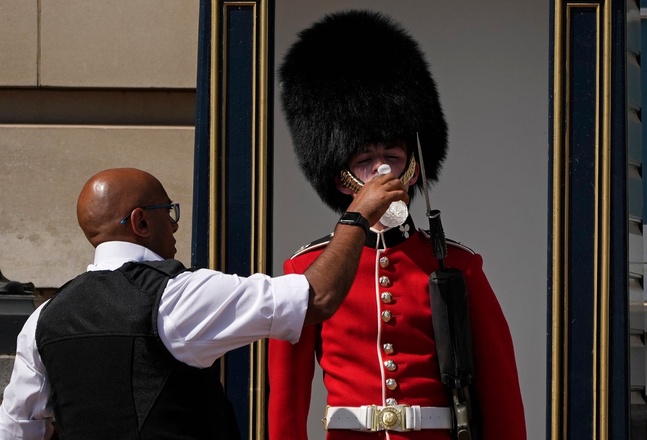 A police officer gives water to a British soldier wearing a traditional bearskin hat, on guard duty outside Buckingham Palace, during hot weather in London on Monday.