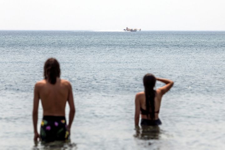 Δύο άνθρωποι παρακολουθούν ένα πυροσβεστικό αεροπλάνο να ξαναγεμίζει στη θάλασσα, καθώς βρίσκεται σε εξέλιξη η πυρκαγιά κοντά στο χωριό Βατερά, στο νησί της Λέσβου. Ελλάδα, 25 Ιουλίου 2022. REUTERS/Elias Marcou