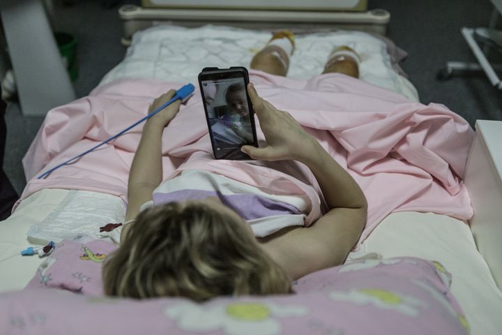 Una niña mira un móvil en una cama de hospital