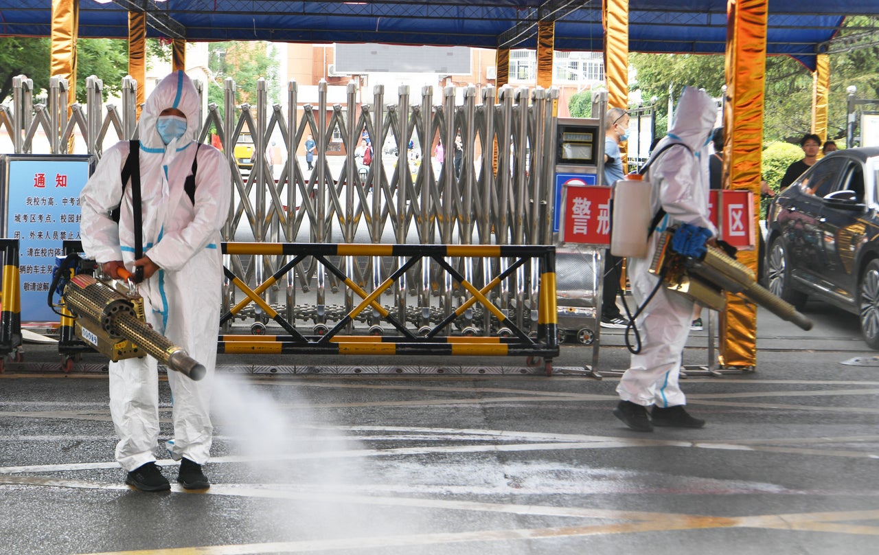 Volunteers wearing personal protective equipment spray disinfectant at an exam site ahead of China's national college entrance exam on June 5, 2022 in Bozhou, Anhui Province of China. (Photo by Zhang Yanlin/VCG via Getty Images)