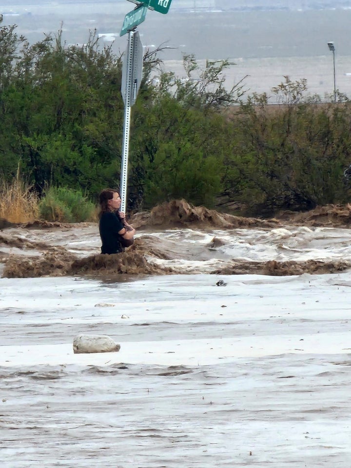 In this photo provided by the Mohave County Sheriff's Office, a woman clings to a stop sign after her car was swept away in Golden Valley, Arizona, on Monday, July 25, 2022.