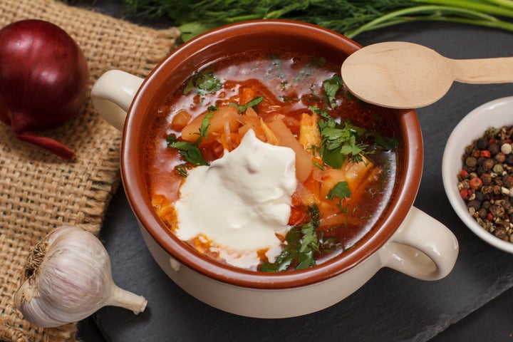 Ukrainian traditional borsch with sour cream in porcelain bowl with spoon, parsley, onion, garlic on sackcloth and stone board. Top view.