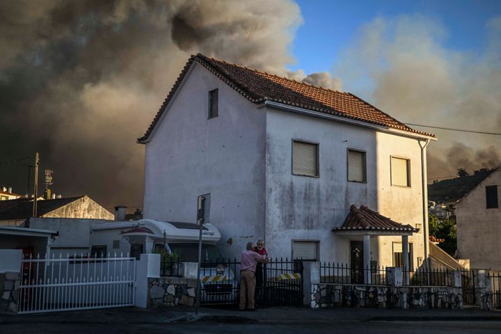 People stand outside their homes watching the progress of a forest fire in Mafra on July 31, 2022.