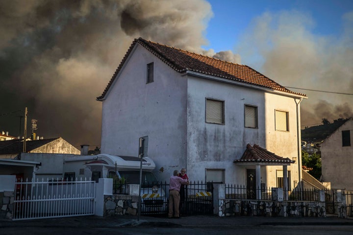 People stand outside their houses watching the progression of a wildfire in Mafra on July 31, 2022.