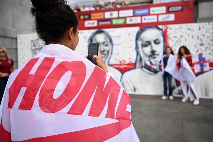 An England fan takes a photograph of friends in front of a mural of Fran Kirby and Leah Williamson.