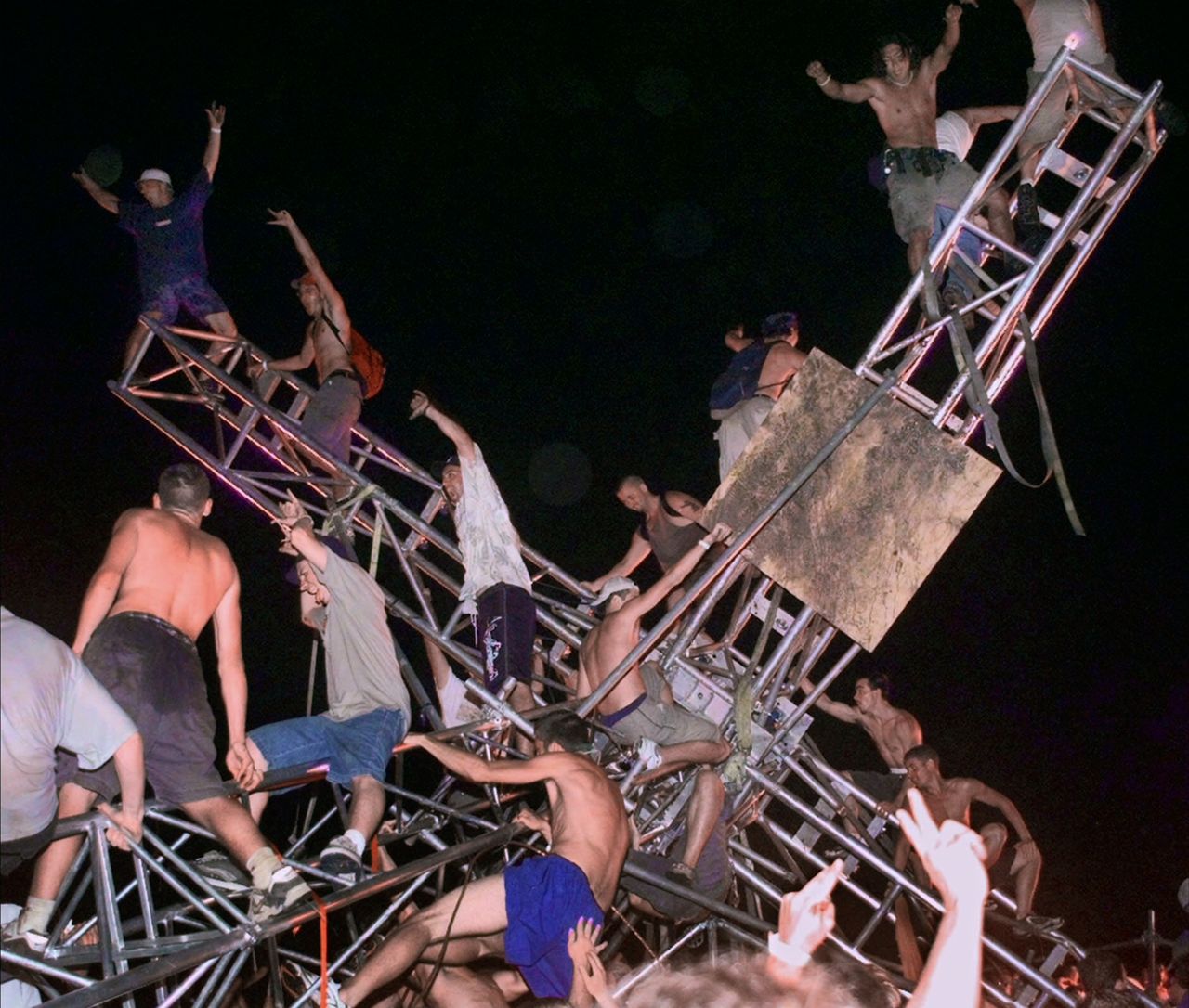 A group of young men climb to the top of a sound tower and flip it over in music festival footage shown in "Trainwreck: Woodstock '99."