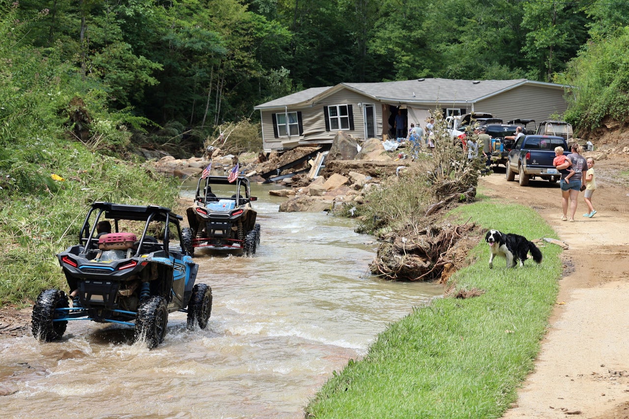 ATV drivers ferrying generator fuel and water drive around Jessica Willett's home, which was torn from its foundations during flooding and left in the middle of the road, along Bowling Creek, on July 31.