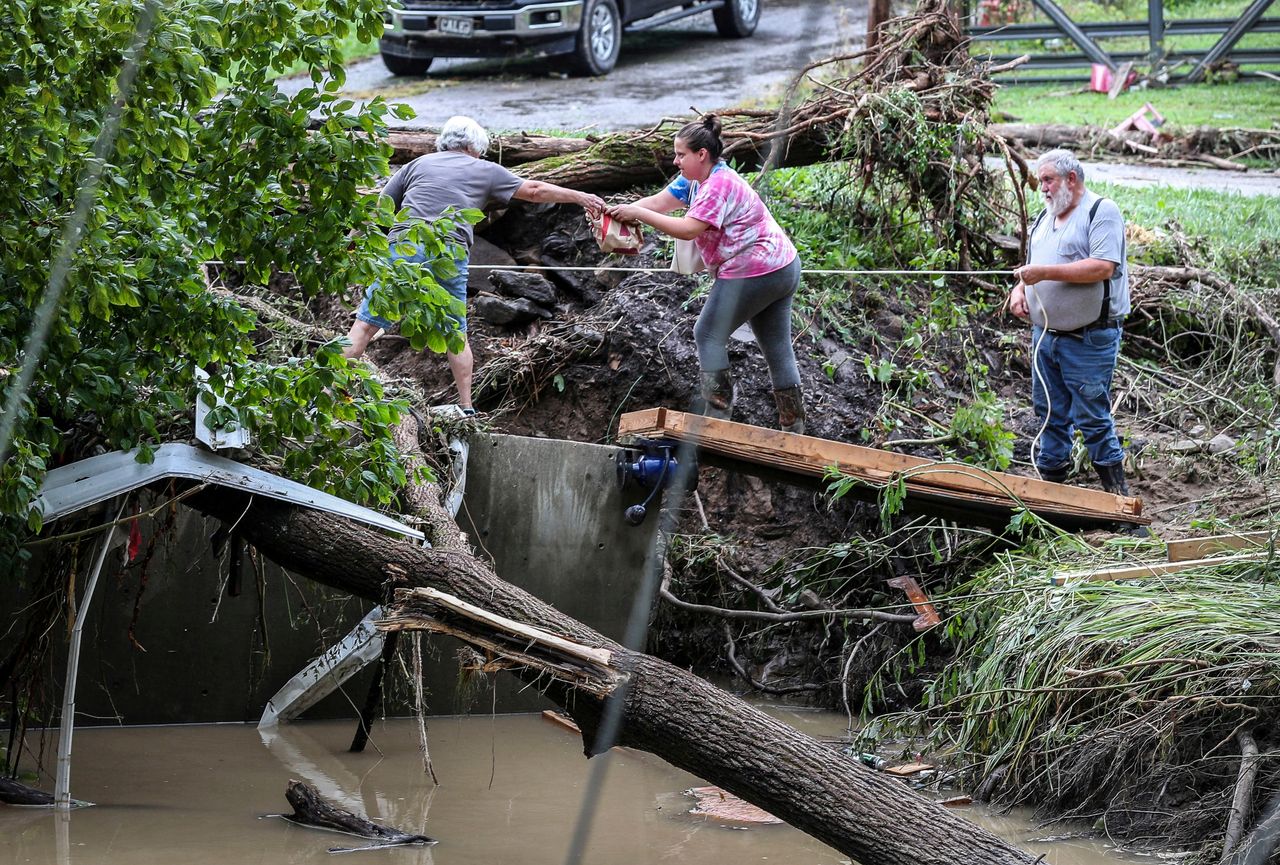 Tonya Smith, whose trailer was washed away by flooding, reaches for food from her mother Ollie Jean Johnson to give to Smith's father, Paul Johnson, as the trio used a rope to hang on over a swollen Grapevine Creek in Perry County, Kentucky, on July 28.