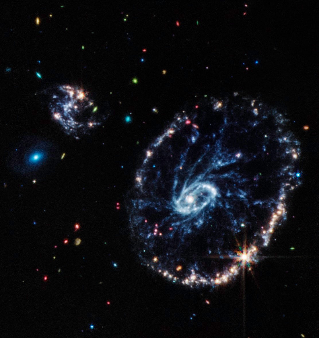 Cette image de l'instrument à infrarouge moyen de Webb (MIRI) montre un groupe de galaxies, dont une grande galaxie en forme d'anneau déformé connue sous le nom de Cartwheel.  La galaxie Cartwheel, située à 500 millions d'années-lumière dans la constellation du Sculpteur, est composée d'un anneau intérieur brillant et d'un anneau extérieur actif.  Alors que cet anneau extérieur a beaucoup de formation d'étoiles, la zone poussiéreuse entre les deux révèle de nombreuses étoiles et amas d'étoiles. La lumière infrarouge moyenne capturée par MIRI révèle des détails fins sur ces régions poussiéreuses et les jeunes étoiles de la galaxie Cartwheel, qui sont riches en les hydrocarbures et autres composés chimiques, ainsi que la poussière de silicate, comme une grande partie de la poussière sur Terre. Les jeunes étoiles, dont beaucoup sont présentes en bas à droite de l'anneau extérieur, dynamisent la poussière d'hydrocarbures environnante, la faisant briller en orange.  D'autre part, la poussière clairement définie entre le noyau et l'anneau extérieur, qui forme les rayons qui inspirent le nom de la galaxie, est principalement de la poussière de silicate.  La plus petite galaxie spirale en haut à gauche de Cartwheel affiche une grande partie du même comportement, montrant une grande quantité de formation d'étoiles.