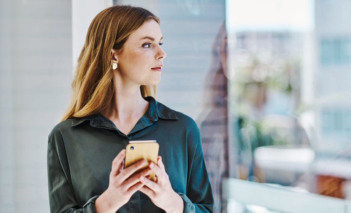 Caucasian businesswoman looking thoughtfully out the window while using a cellphone in an office