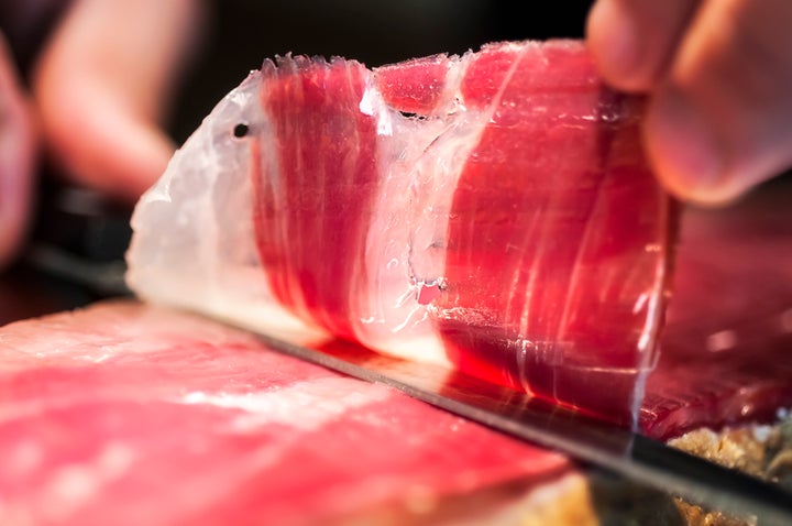 Close up of hand and knife cutting jamon iberico in Spain.