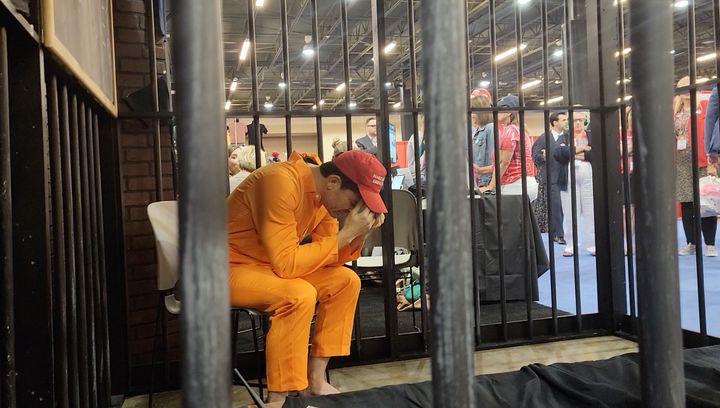 CPAC attendees look at a bizarre exhibit in which an actor, pretending to be a Jan. 6 rioter, sobs in a jail cell.