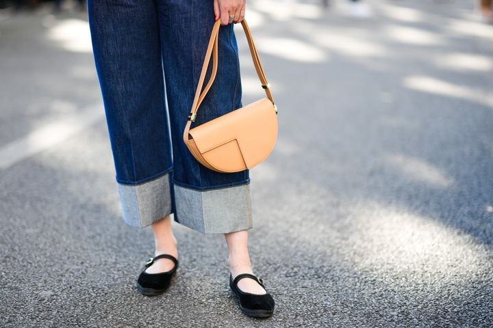 A Paris Fashion Week attendee wears navy blue, denim rolled-up jeans; a brown shiny leather handbag and black velvet ballet pumps.