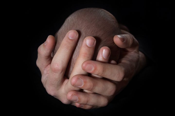 Imagen de unas manos sujetando la cabeza de un bebé.