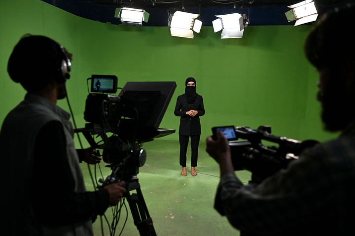 In this photograph taken on May 28, 2022, an Afghan female presenter with news network 1TV, Lima Spesaly (C) with her face covered by a veil, speaks during a live broadcast at the 1TV channel station in Kabul. - After initially defying the Taliban order to cover their faces on air, Afghan women television presenters are broadcasting news and other programmes wearing masks. Spesaly, said it was difficult to work like this for hours but vowed to fight for her rights and of other Afghan women that are being increasingly crushed by the hardline Islamist rulers.