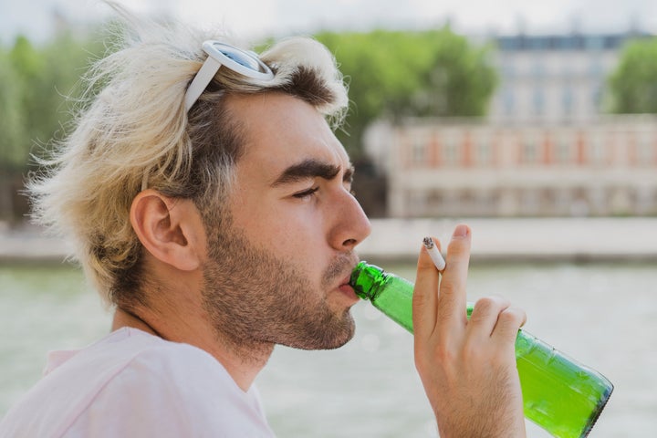 Imagen de archivo de un joven bebiendo cerveza mientras que fuma un cigarrillo.