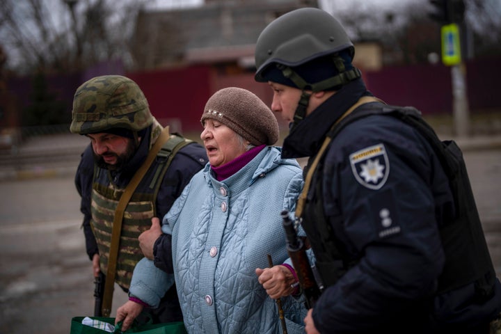 FILE - Ukrainian police officer Ruslan Huseinov, left, with his colleague help a woman fleeing as the artillery echoes nearby in Irpin, in the outskirts of Kyiv, Ukraine, on March 7, 2022.