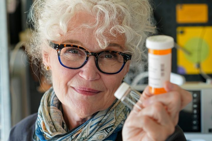 Mary Beth Orr poses for a photo in her home, Tuesday, Aug. 23, 2022 in Burien, Wash., south of Seattle, while holding medicine bottles used to give her doses of psilocybin, the compound in psychedelic mushrooms, as part of a study to try and help heavy drinkers cut back or quit entirely. Orr used to have five or six drinks every evening and more on weekends before she enrolled in the study in 2018. She stopped drinking entirely for two years, and now has an occasional glass of wine, and credits psilocybin for her progress. (AP Photo/Ted S. Warren)