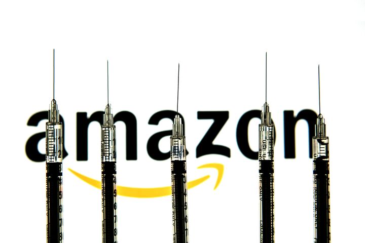 FILE: Medical syringes are seen with an Amazon logo in the background. Amazon has announced the end of its virtual health service that it launched in 2019.