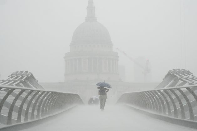 ミレニアム・ブリッジを雨の中渡る人。数週間にわたる暑さの後、ロンドンは集中豪雨に見舞われた（2022年8月17日、イギリス・ロンドンで撮影）