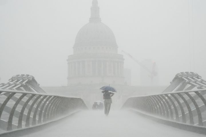 ミレニアム・ブリッジを雨の中渡る人。数週間にわたる暑さの後、ロンドンは集中豪雨に見舞われた（2022年8月17日、イギリス・ロンドンで撮影）