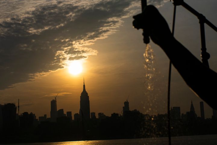 Ο ήλιος ανατέλλει πάνω από την πόλη της Νέας Υόρκης και το Empire State Building ενώ ένας άνδρας ψεκάζει νερό στην προβλήτα A το Σάββατο 20 Ιουλίου 2019 στο Hoboken, N.J.