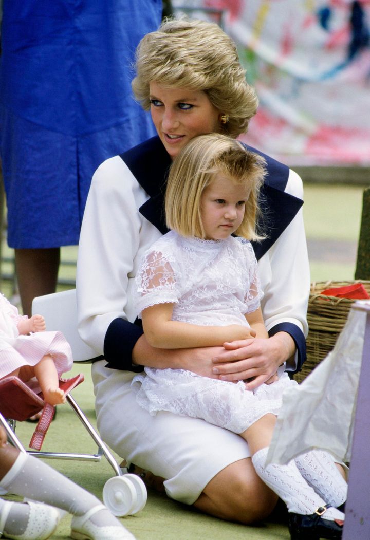Diana sentada en el suelo y con una niña en su regazo durante un tour en Australia en los 80.