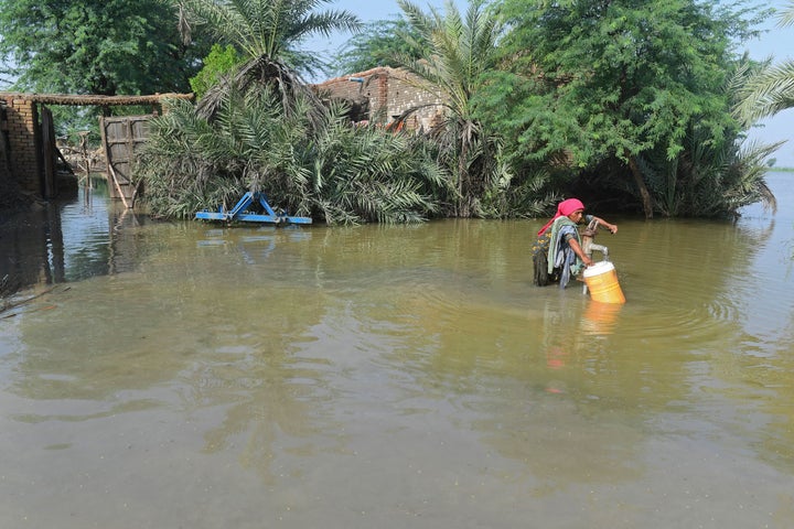 A flood affected woman fills drinking water from a partially submerged handpump near by her flooded house at Shikarpur in Sindh province