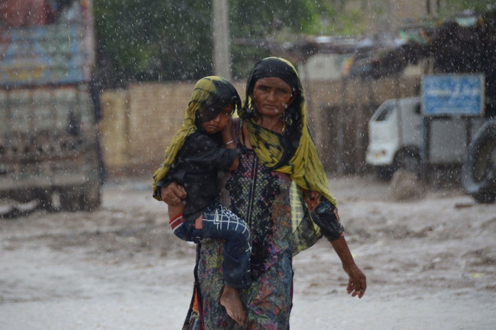 A woman carrying a child walks along a street during a heavy rainfall in the flood hit Dera Allah Yar town in Jaffarabad district, Balochistan province.