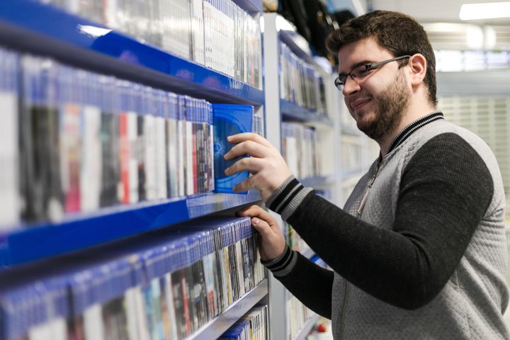 A happy man, selecting a DVD at a video store, not yet aware of the shame he will soon endure.