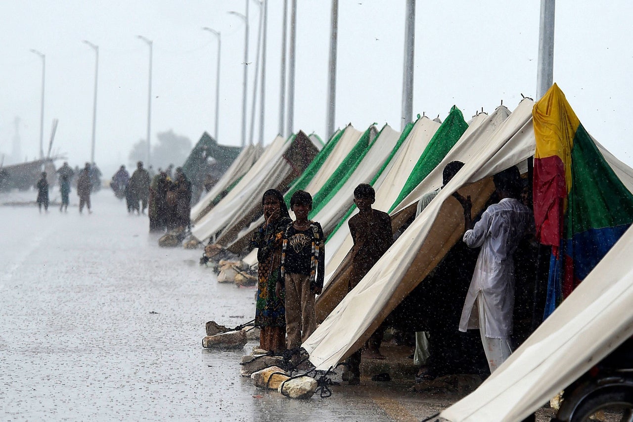 People who fled their flood hit homes stand outside temporary tents set along a road during a heavy monsoon rainfall in Sukkur of Sindh province, on Aug. 27, 2022.