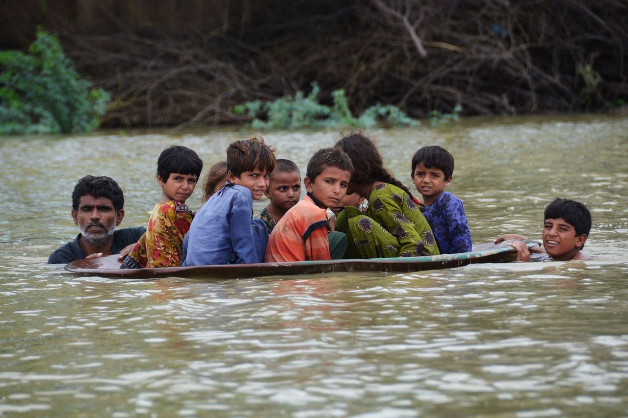 A man (L) along with a youth use a satellite dish to move children across a flooded area after heavy monsoon rainfalls in Jaffarabad district, Balochistan province, on Aug. 26, 2022. Heavy rain continued to pound parts of Pakistan on August 26 after the government declared an emergency to deal with monsoon flooding it said had "affected" over 4 million people.