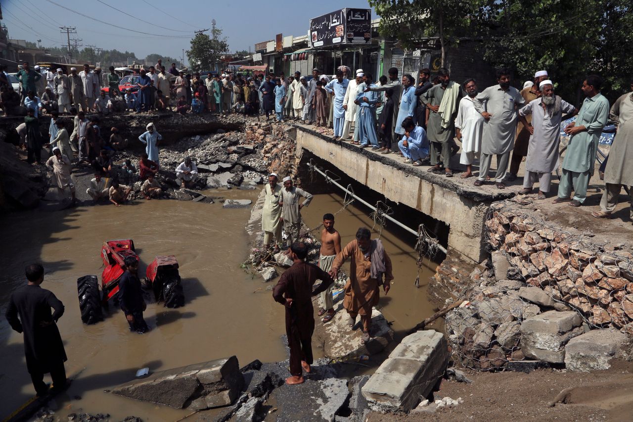 People stand around a washed-out road after heavy rains in Charsadda, Pakistan, on Aug. 30, 2022.