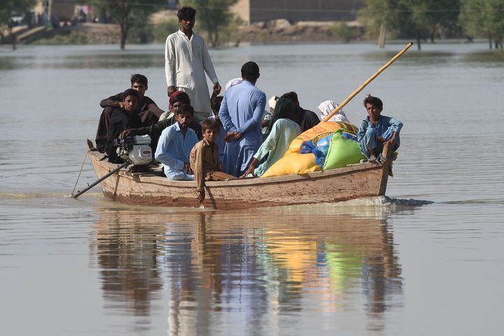 Flood-affected people use a boat to return to their homes with relief food bags in the flooded area following heavy monsoon rains in Rajanpur district of Punjab province on September 4, 2022.