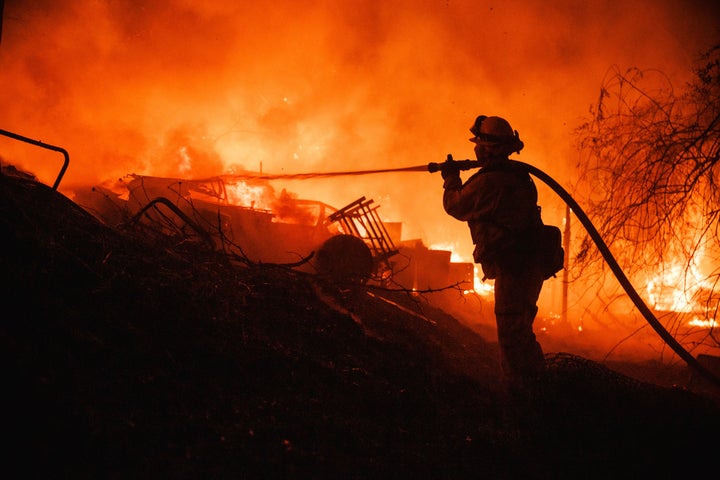 A firefighter takes a hose to a burning property while battling the Fairview Fire on Sept. 5, 2022, near Hemet, Calif. 