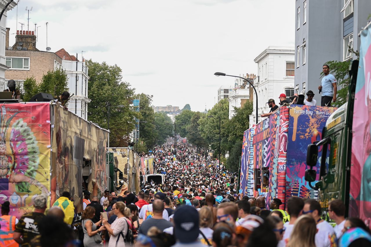 Millions of attendees walk along the parade route at Notting Hill Carnival, alongside floats.