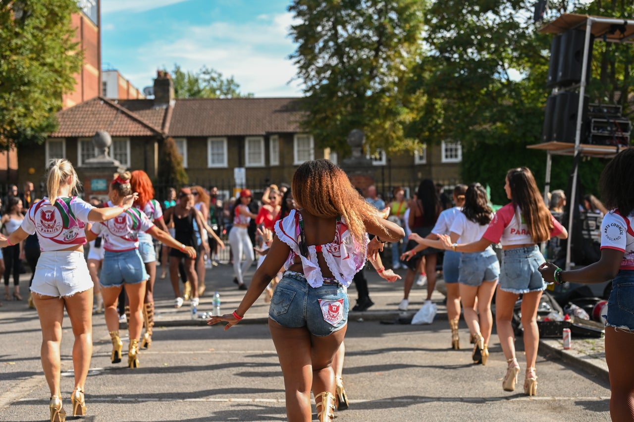 Students from the Paraiso School of Samba rehearse the day before the Notting Hill Carnival parade, as onlookers watch.