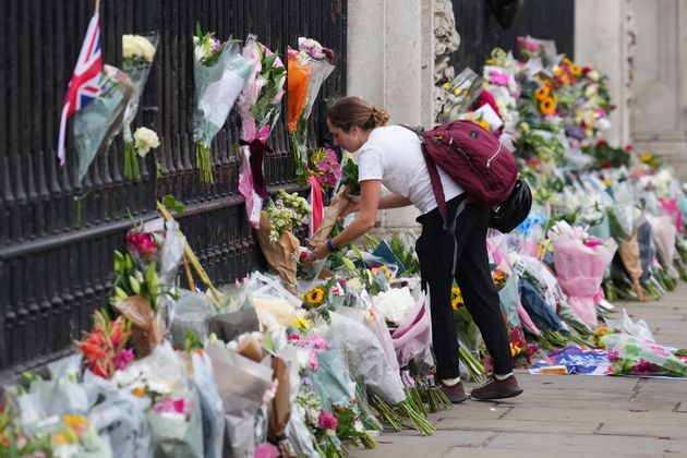 A woman pauses next to flowers and tributes to Queen Elizabeth II outside Buckingham Palace on September 9, 2022.