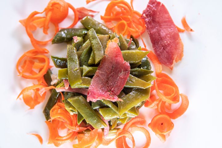 A vegetable dish based on green beans with fried ham and a side of carrot.
