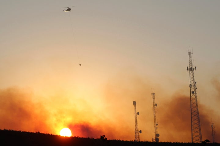 A helicopter carries water on a longline to a wildfire near Salem, Oregon, at sunset Friday, Sept. 9, 2022.