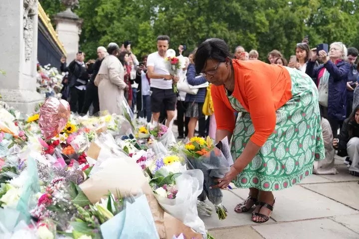 Una mujer deja un ramo de flores frente a Buckinham Palace.