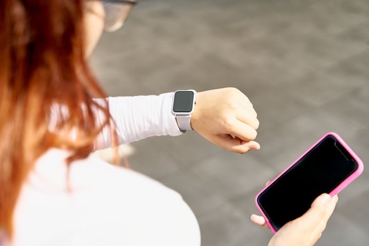 Teenager with long hair wear white shirt and she looks at her smartwatch while holding a cell phone with other hand