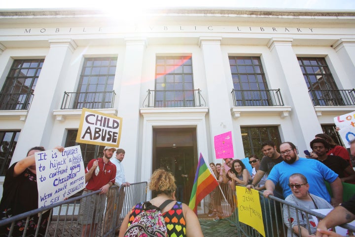 A parent walks their child past protesters and into the Mobile Public Library for drag queen storytime in 2018.