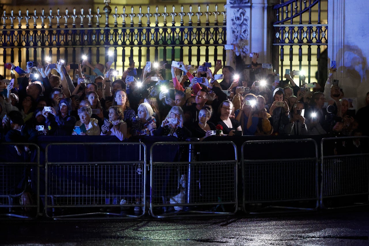 Members of the public are lit by their mobile phones as they await the arrival of the hearse.