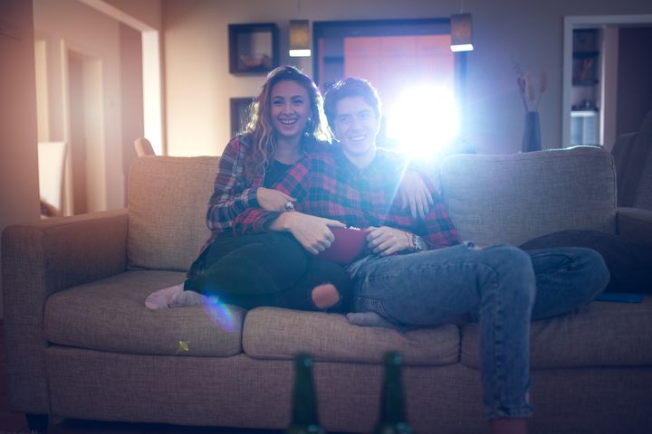 A couple sitting on a couch with a projector behind them