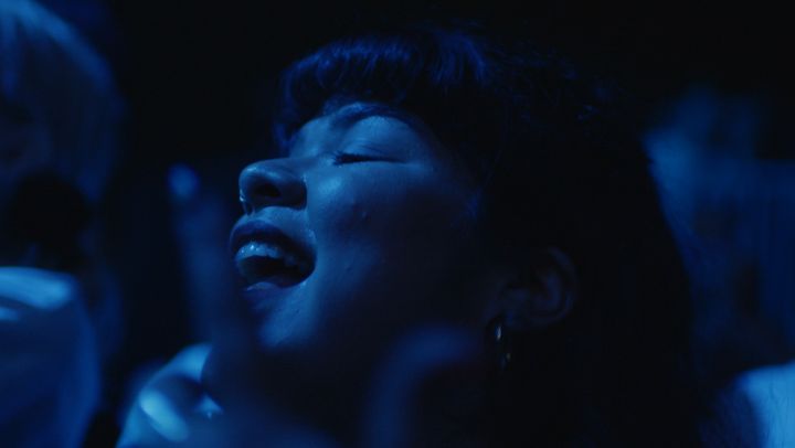 Musician and music manager Doris Muñoz dances in a blue-lit crowd at a concert in New York City, in a scene from the documentary "Mija."