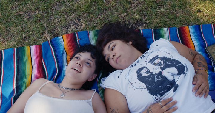 Doris Muñoz and Jacks Haupt lay on a multicolored blanket in the grass, in a scene from the documentary "Mija."